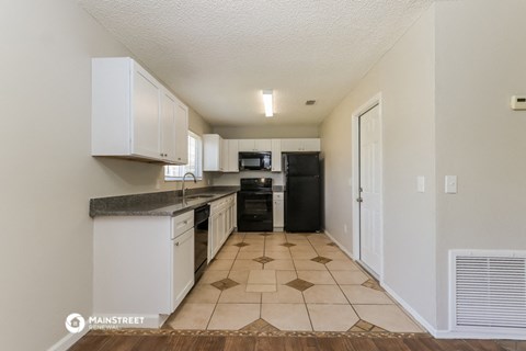 a kitchen with white cabinets and a black refrigerator and a sink