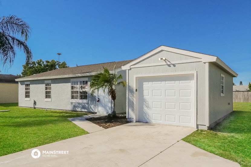 a gray house with a white garage and a palm tree