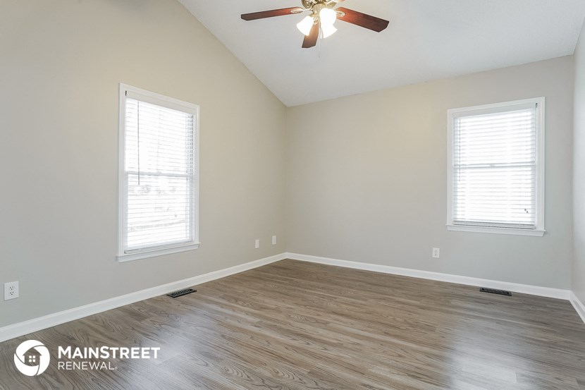 an empty room with a ceiling fan and two windows