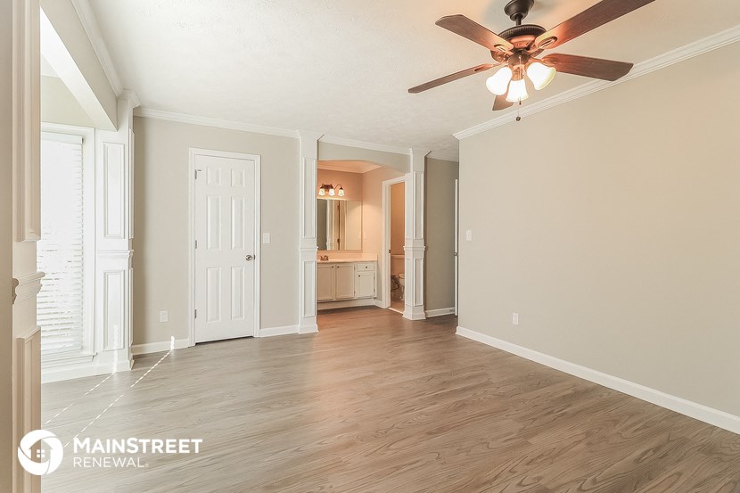 an empty living room with a ceiling fan and a door to a bathroom