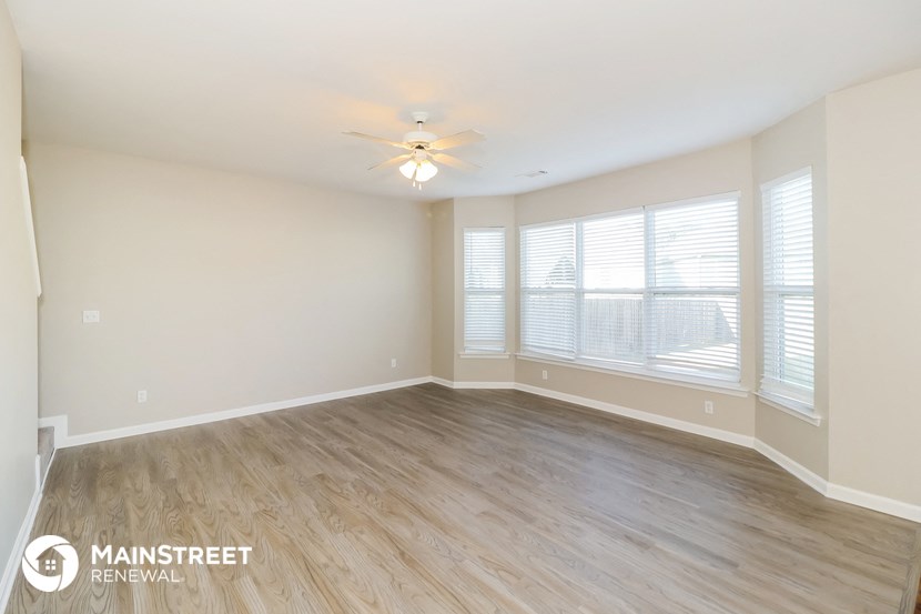 the spacious living room with wood flooring and a ceiling fan