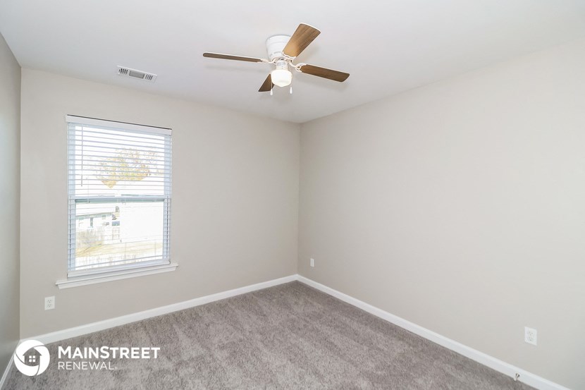 the living room of an apartment with carpet and a ceiling fan