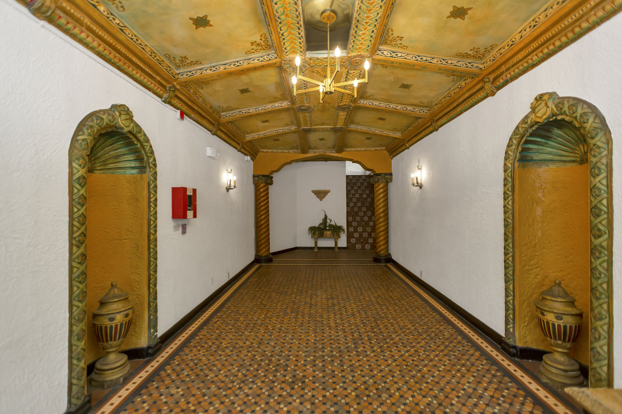 A hallway with a patterned floor and a chandelier hanging from the ceiling.