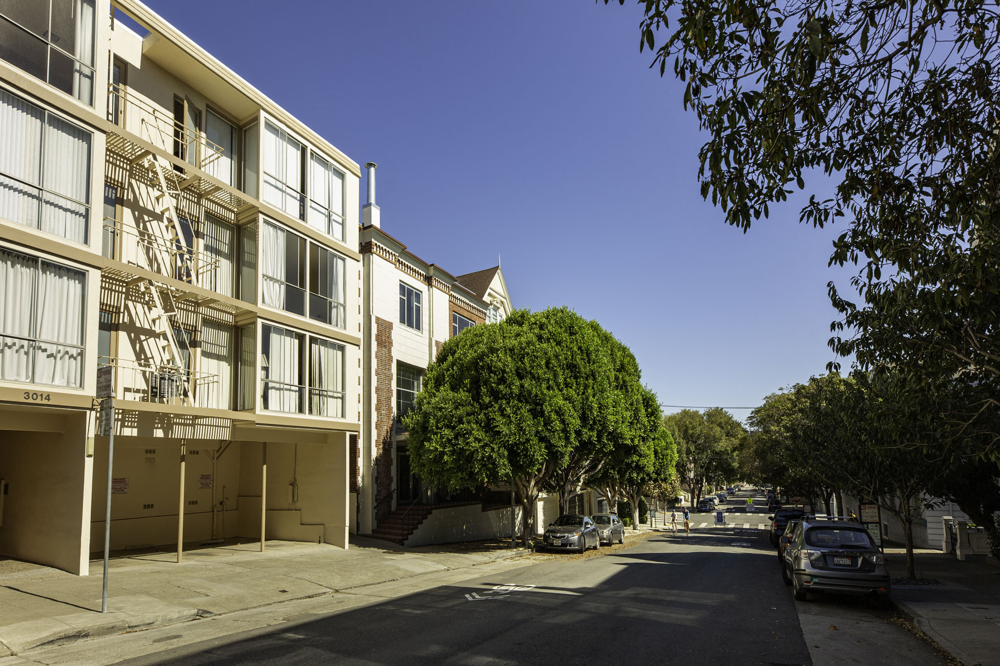 A street view of a residential area with apartment buildings and parked cars.