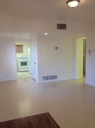 an empty living room with a kitchen in the background