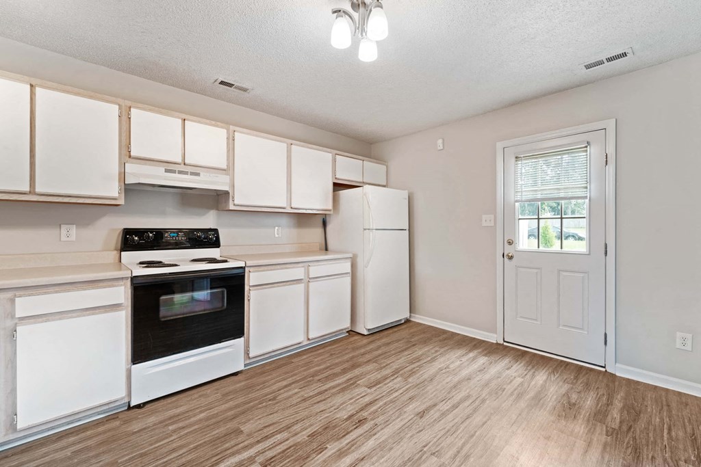 an empty kitchen with white cabinets and appliances and a door