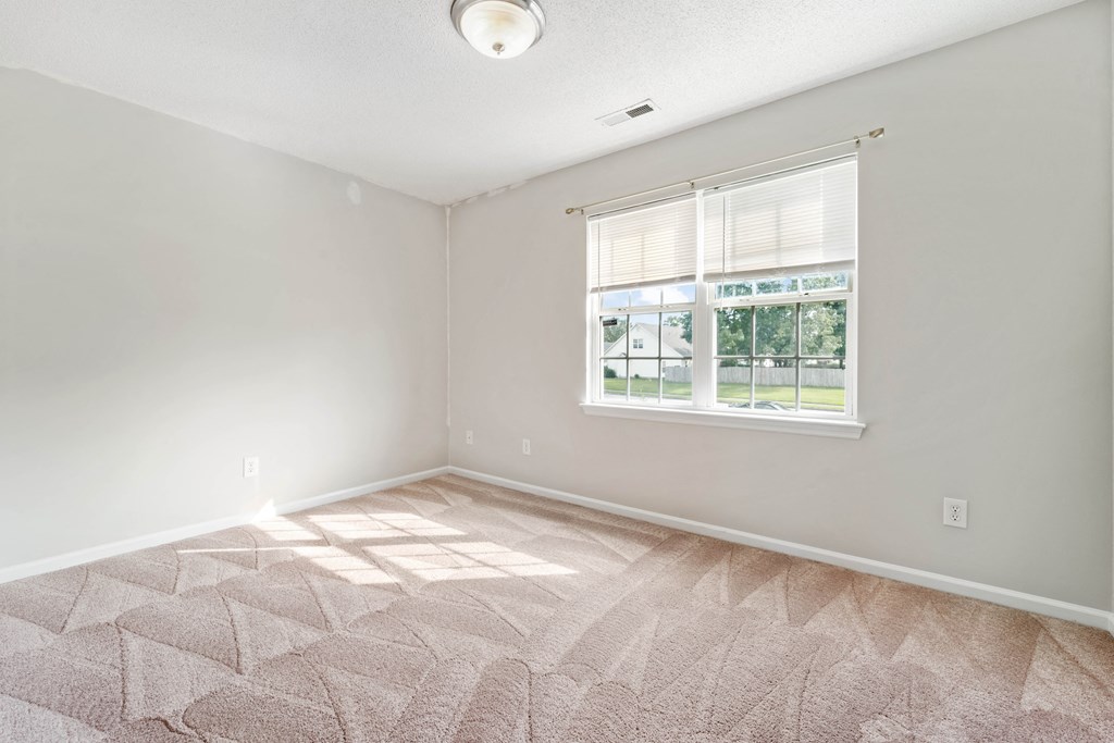 an empty bedroom with a window and a carpeted floor