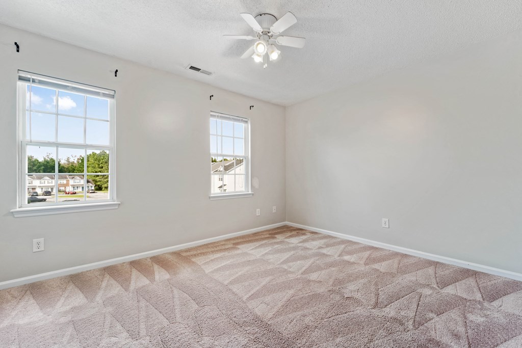 an empty living room with two windows and a ceiling fan