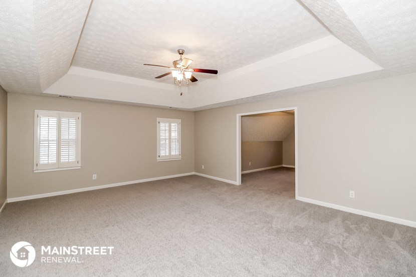 the spacious living room with ceiling fan and carpet