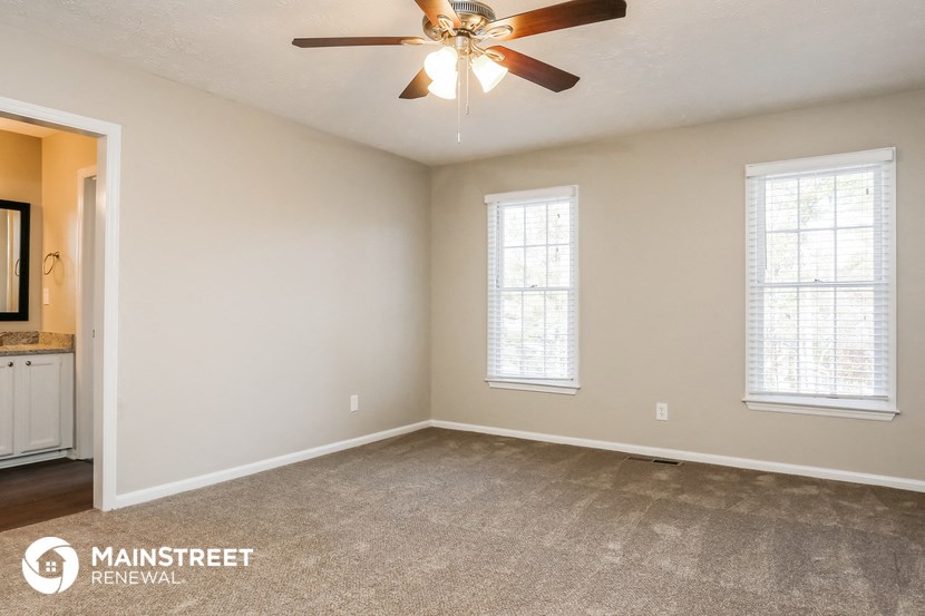 the spacious living room with carpeted floors and a ceiling fan