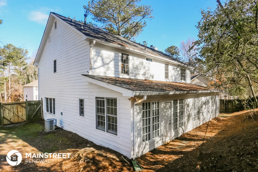the back of a white house with a fence and trees