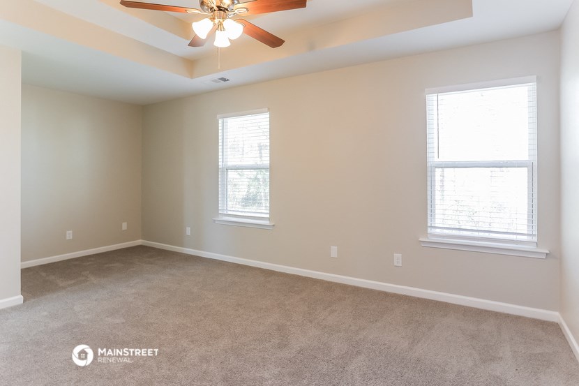 an empty living room with a ceiling fan and two windows