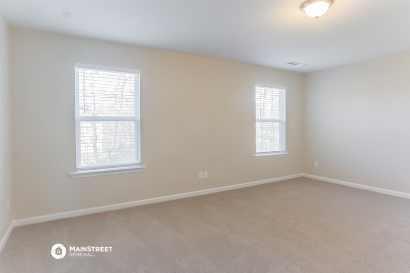 the spacious living room with two windows and beige carpeting