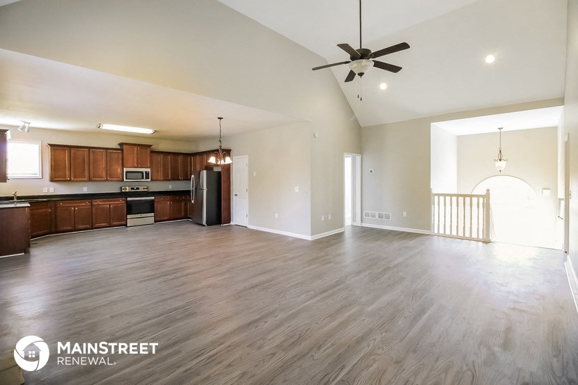 an empty living room and kitchen with wood flooring and a ceiling fan