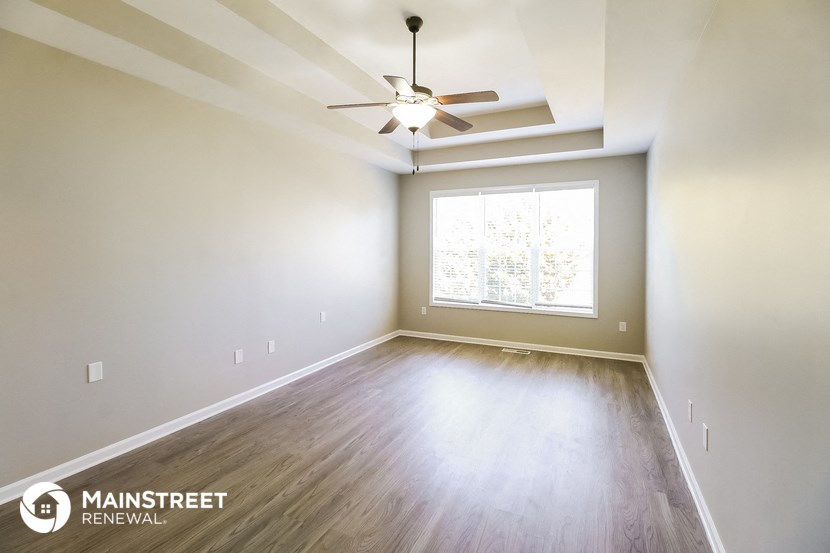 the spacious living room with wood floors and a ceiling fan