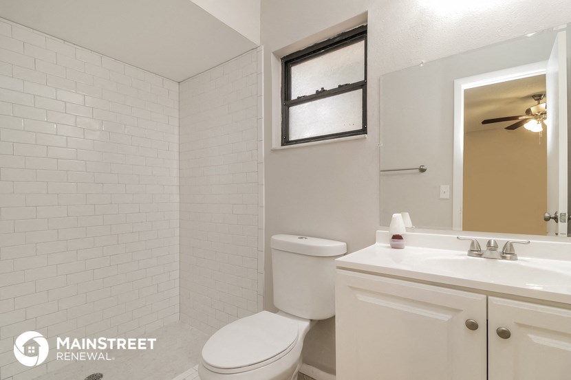 a white tiled bathroom with a toilet sink and mirror