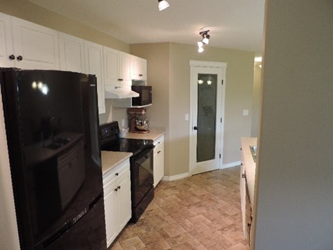 A black refrigerator in a kitchen with white cabinets.