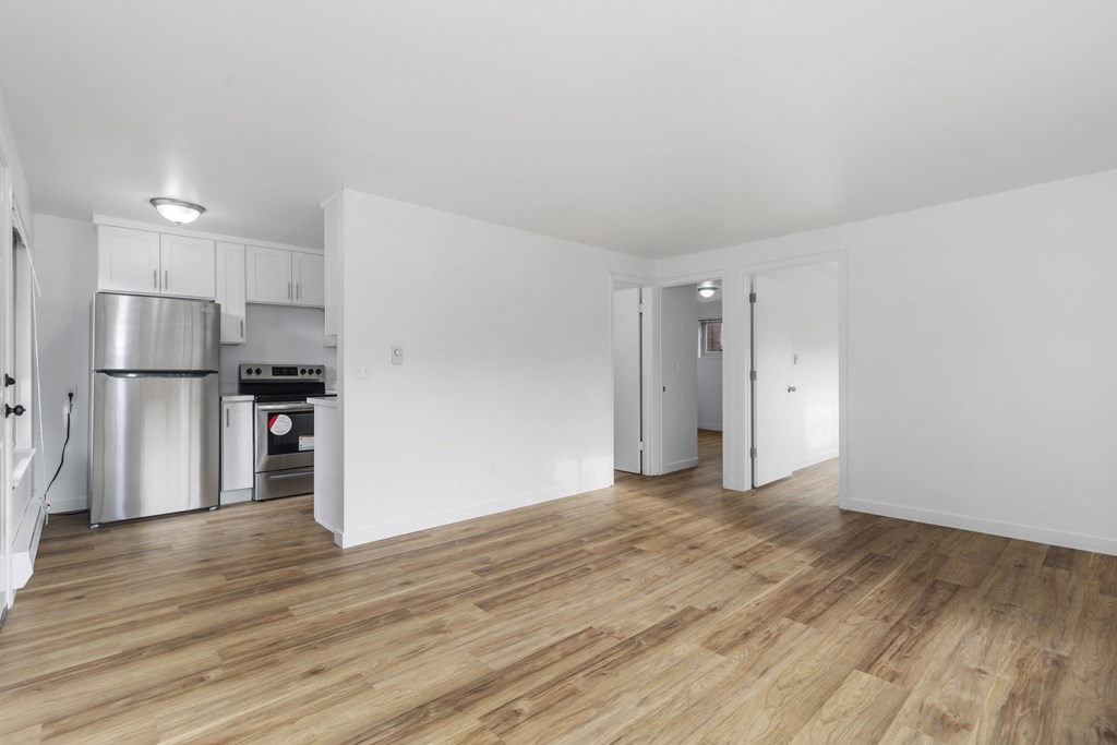 the living room and kitchen of an apartment with white walls and wood floors