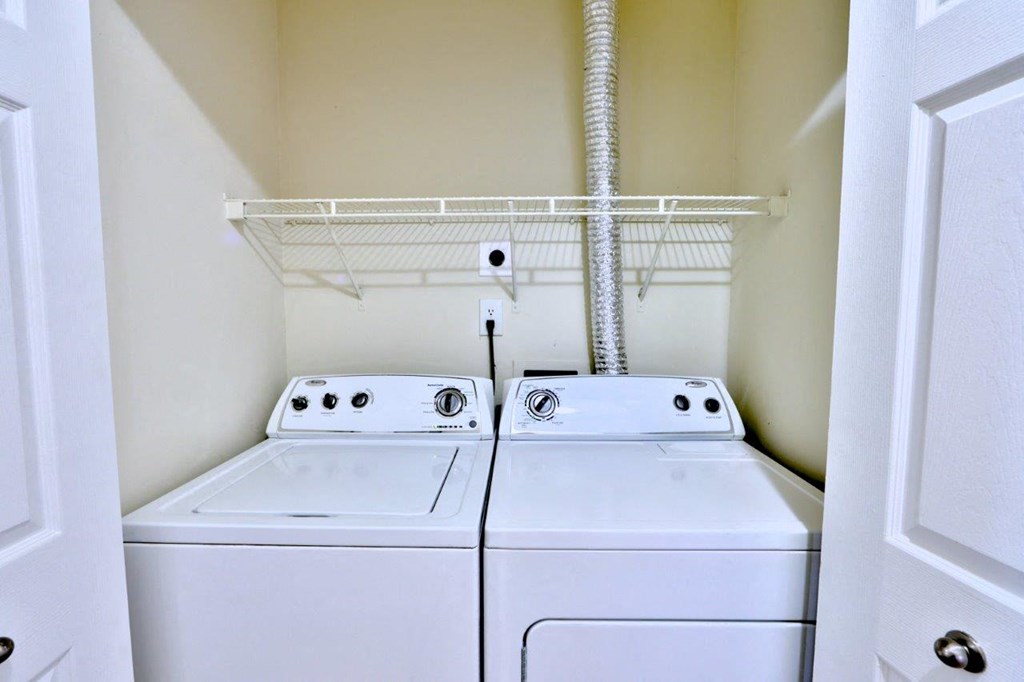 two washers and dryers in a closet with a shelf above them