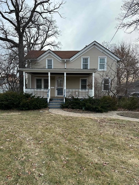 A house with a porch and a tree in front.