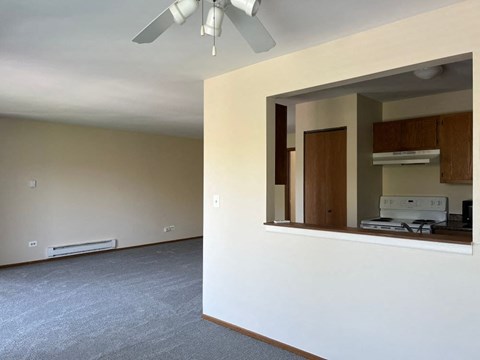 A room with a ceiling fan and a window with a view of a kitchen.