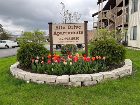 A sign for Alta Drive Apartments is surrounded by a flower bed.