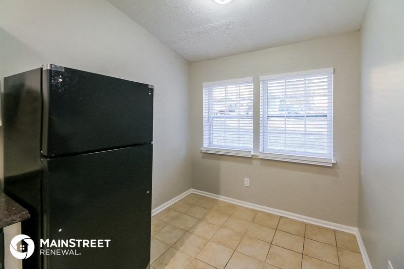 an empty kitchen with a refrigerator and two windows