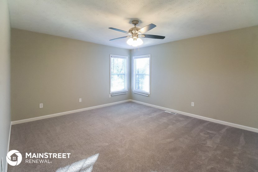 an empty living room with a ceiling fan and two windows