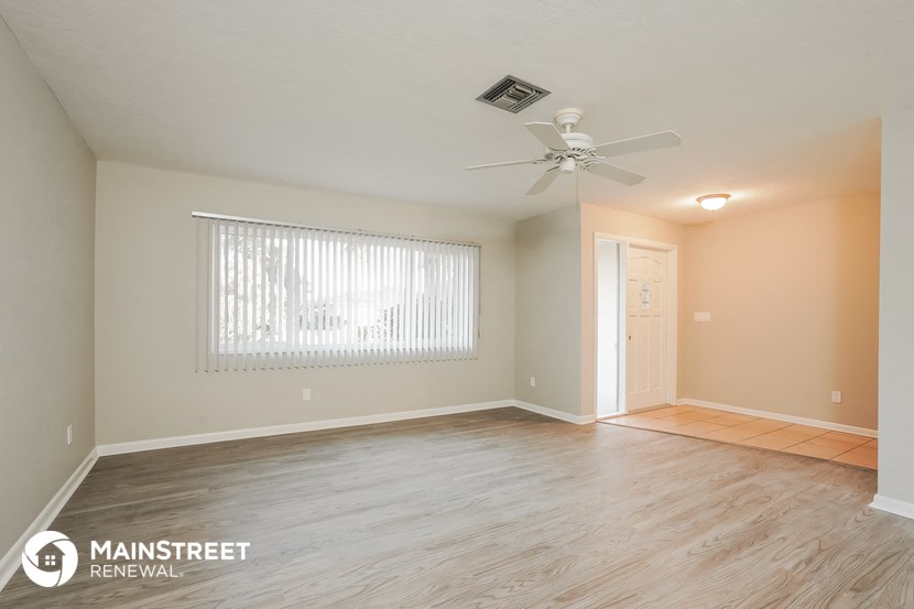 the spacious living room with wood flooring and a ceiling fan