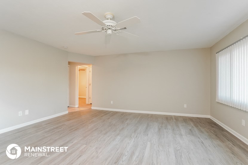 the spacious living room with wood flooring and a ceiling fan