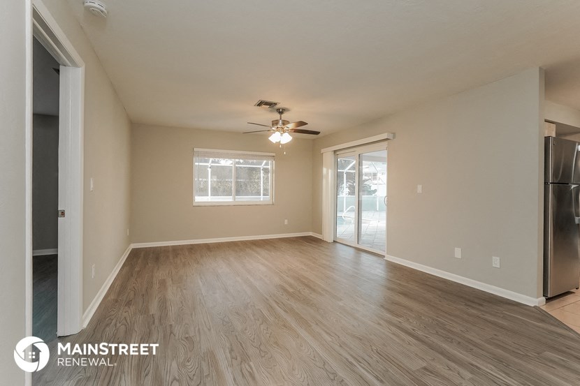 the living room of an apartment with wood flooring and a ceiling fan