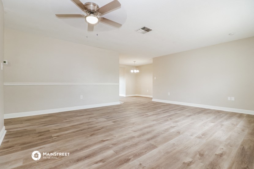 the spacious living room with wood flooring and a ceiling fan