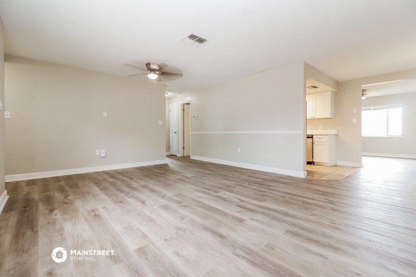 the spacious living room with wood flooring and a ceiling fan