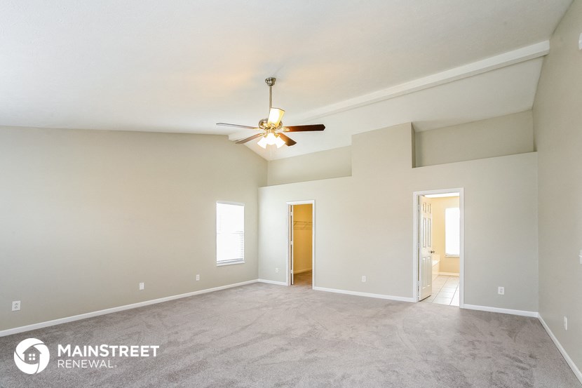 the spacious living room with ceiling fan and carpeting