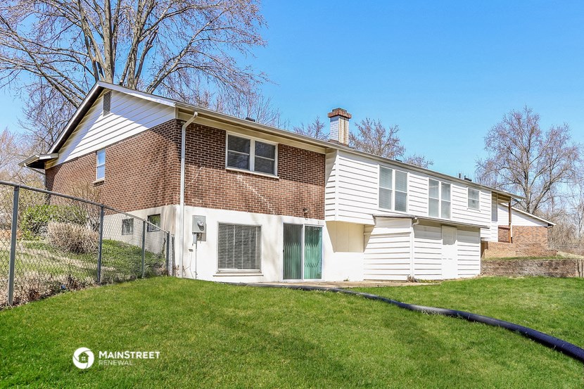 a white and brick house with a yard and a chain link fence