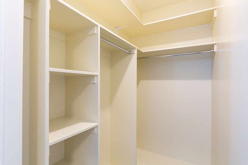 a walk in closet with white shelves and a glass door