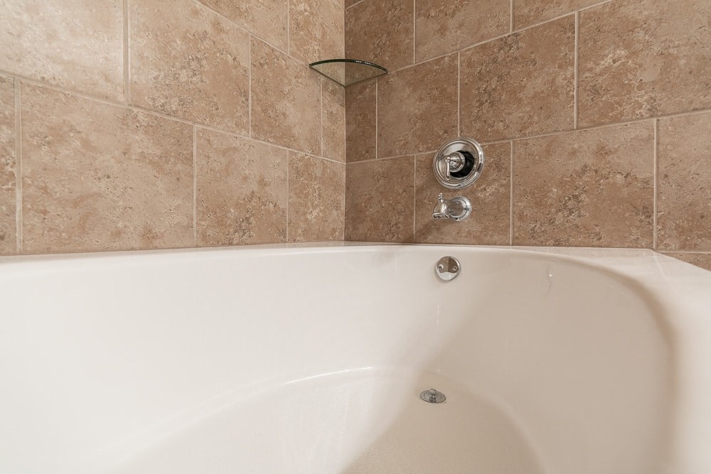 a white bath tub in a bathroom with brown tiles