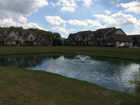 A pond in front of a row of houses with a fountain in the middle.