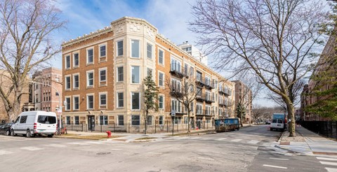 A street view of a large brick building with a white van parked in front.