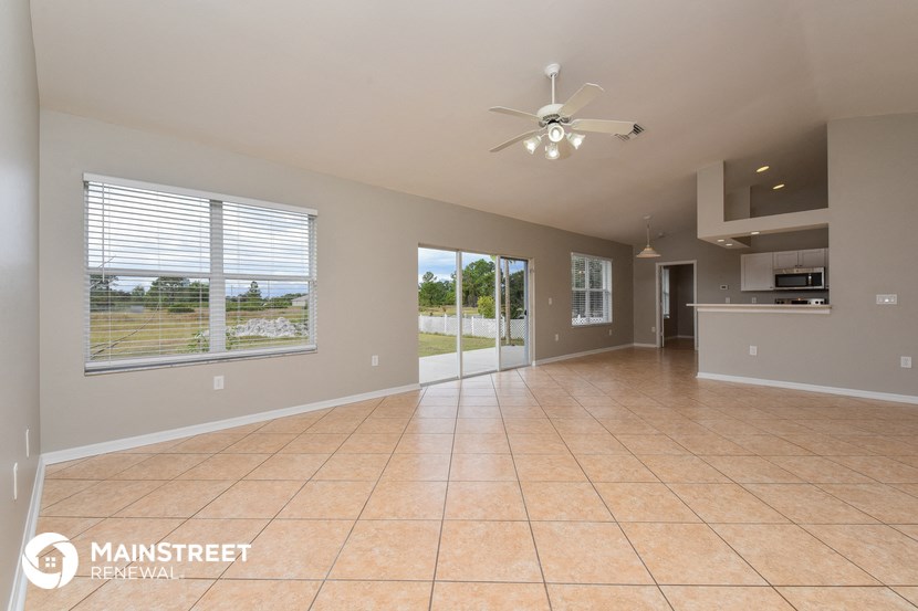 an empty living room with a kitchen and a ceiling fan