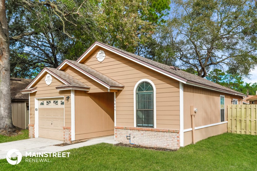 a small tan house with a garage and a tree