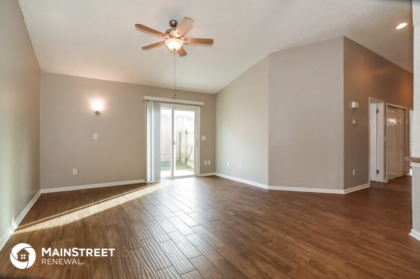 the spacious living room with hardwood flooring and a ceiling fan