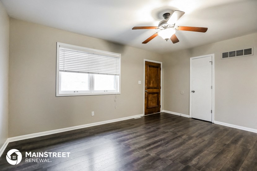 the spacious living room with wood floors and a ceiling fan
