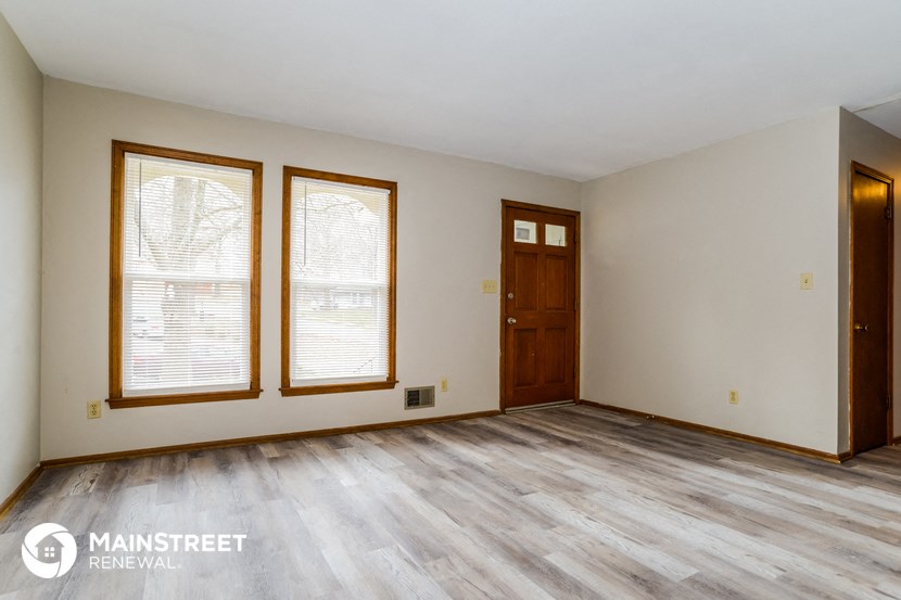 the living room of a home with wooden floors and white walls