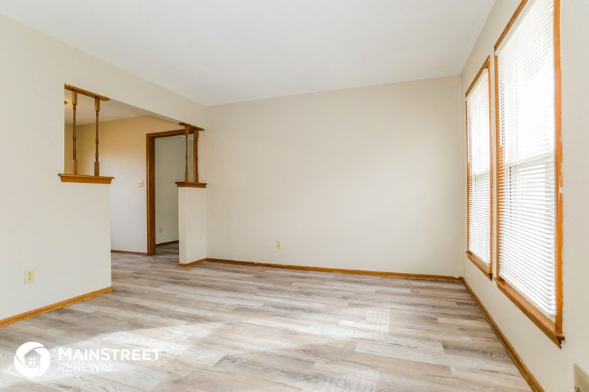 the living room of a home with white walls and wood floors