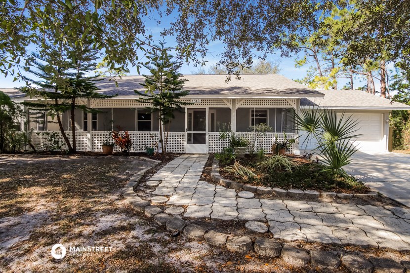 the front of a white house with a stone driveway and trees