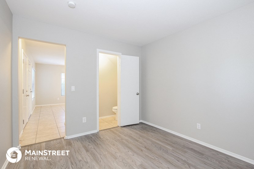 the spacious living room with wood flooring and a hallway to the bathroom
