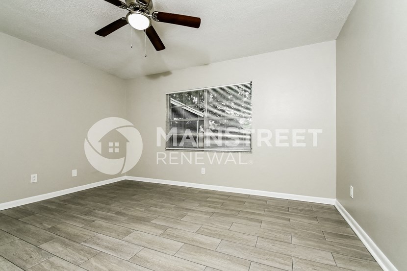 a clean and empty living room with a ceiling fan and a window