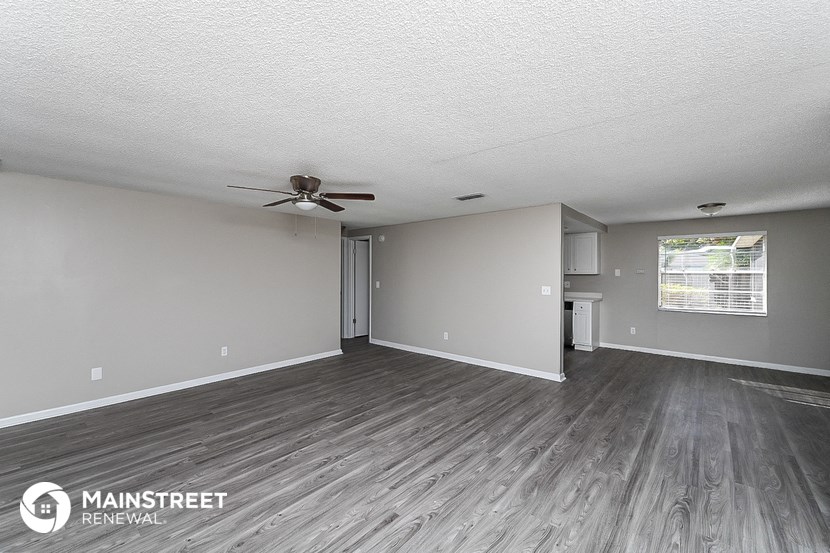 the living room of an apartment with wood flooring and a ceiling fan