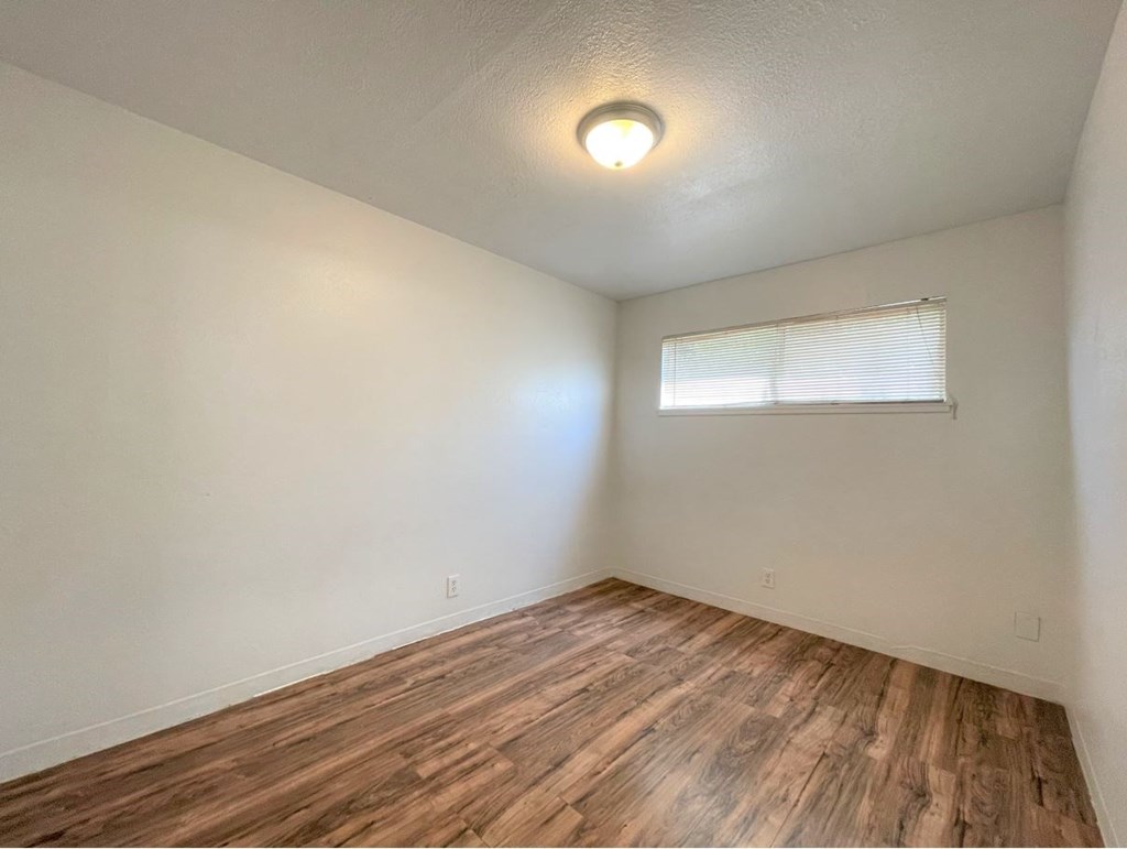 the spacious living room with wood flooring and a window